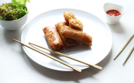 Fried spring rolls on white plate and chopsticks on white background