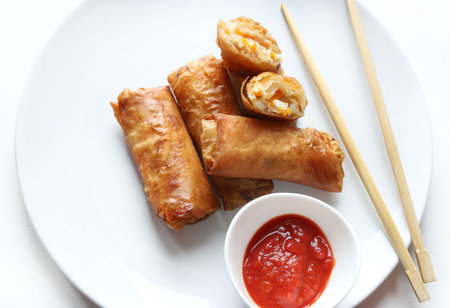Fried spring rolls with sauce and chopsticks on white background.
