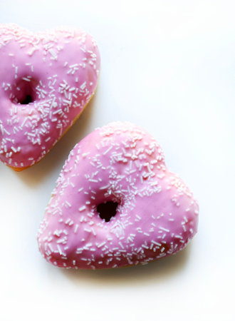 Two heart-shaped donuts with pink icing and sprinkles, isolated on a white background. Romantic or Valentine's Day theme. Overhead view.の写真素材