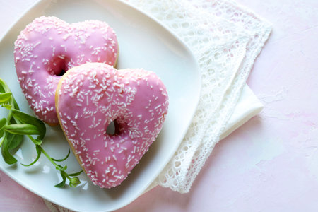 Two heart-shaped donuts with pink icing and sprinkles on a white plate, a light pink background. Romantic or Valentine's Day theme. Copy space.の写真素材