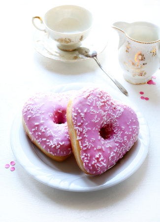 Two heart-shaped donuts with pink icing and sprinkles, served on a white plate, on a white background. Romantic or Valentine's Day theme.の写真素材