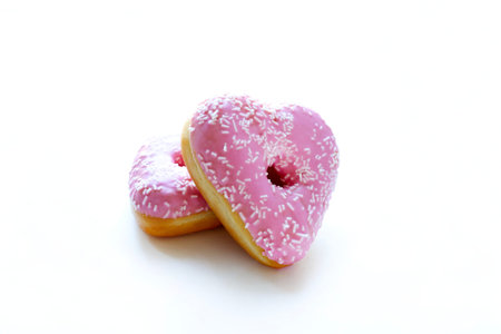 Two heart-shaped donuts with pink icing and sprinkles, isolated on a white background. Romantic or Valentine's Day theme. Overhead view.の写真素材