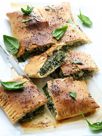 Spanakopita, a traditional Greek savory pie made with phyllo pastry, fresh spinach, and feta cheese, served on a white plate.の写真素材