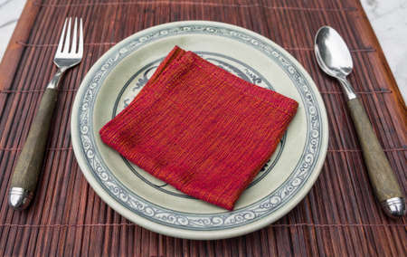 Oriental style table place setting with plate, napkin, and wooden handled spoon and fork on a placematの写真素材