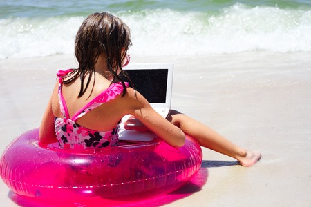 Rear view of little girl using laptop on beachの写真素材