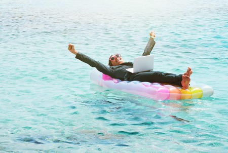 Happy businesswoman resting on lilo with laptopの写真素材