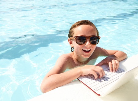 Happy boy using laptop in pool at summer resortの写真素材