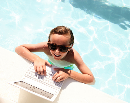 Top view of happy boy with laptop in swimming poolの写真素材