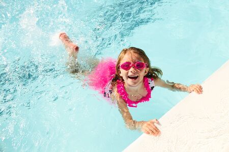 Happy little girl swimming holding on to pool edgeの写真素材