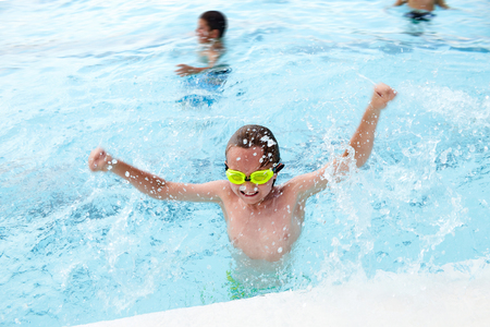 Portrait of happy little Caucasian boy wearing goggles having fun in swimming pool splashing waterの写真素材