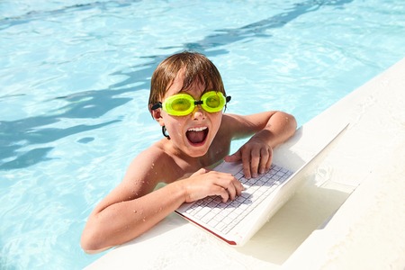 Excited little boy using laptop in swimming poolの写真素材