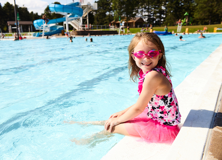 Portrait of happy little girl sitting on pool edgeの写真素材