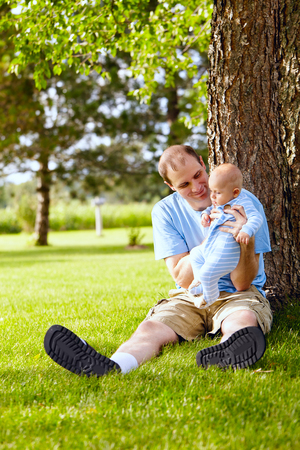 Smiling father playing with newborn son outdoorの写真素材