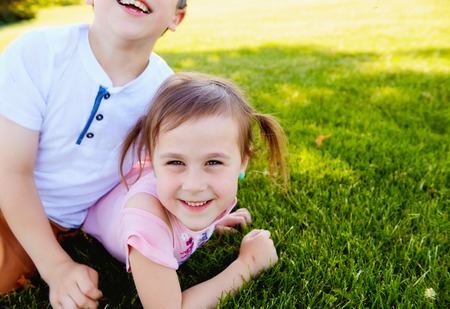 Happy little girl lying on grass with her brotherの写真素材