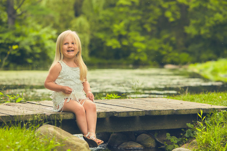 Little girl sitting an wooden bridge and laughingの写真素材