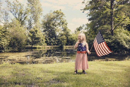 Happy little girl standing with USA flag in parkの写真素材