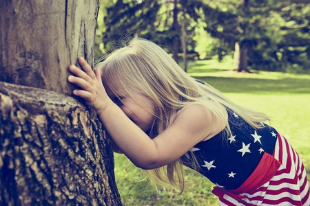 Cheerful little girl hiding behind treeの写真素材