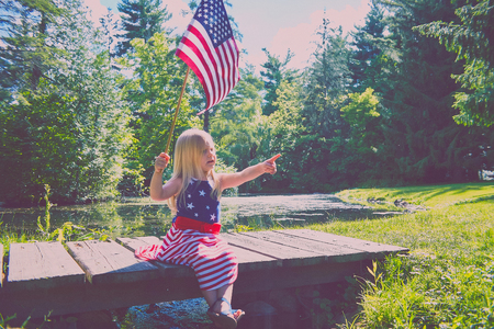Curious girl with usa flag sitting on wooden bridgeの写真素材