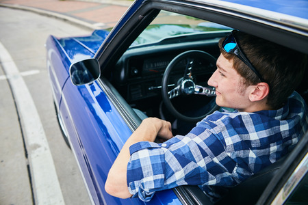 Rear view of young Caucasian man wearing checked shirt sitting in his car looking away and smilingの写真素材