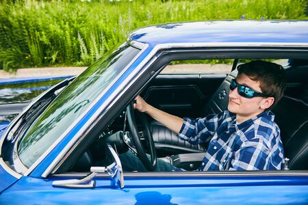 Portrait of cool confident young Caucasian man wearing checked shirt and sunglasses driving his carの写真素材