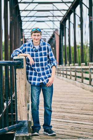 Portrait of happy young Caucasian man wearing checked shirt and sunglasses standing on bridge, looking at camera and smilingの写真素材