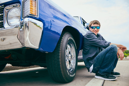 Portrait of happy young Caucasian man wearing sunglasses sitting at his car, looking at camera and smilingの写真素材
