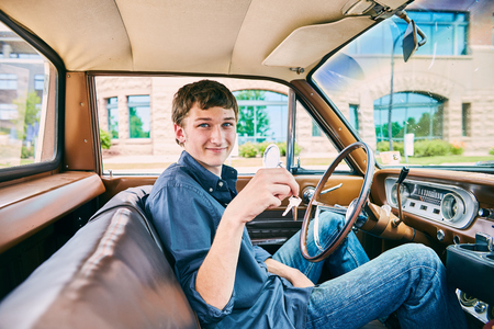 Portrait of happy young Caucasian man sitting in car, holding keys, looking at camera and smilingの写真素材
