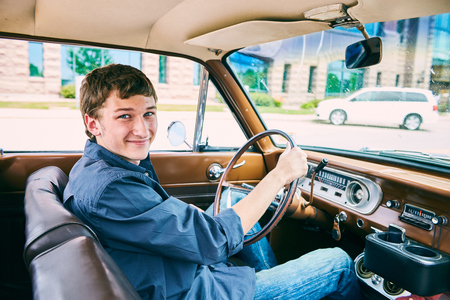 Portrait of happy Caucasian teenage boy driving car, looking at camera and smilingの写真素材