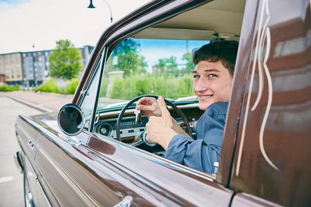 Face of happy male driver sitting in car, showing keys in car window, looking at camera and smiling