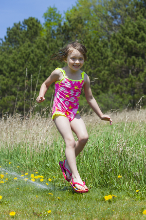 Joyful girl playing with sprinkle water outside and having fun. Summer conceptの写真素材