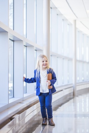 Portrait of little blond girl standing at window in office hallの写真素材