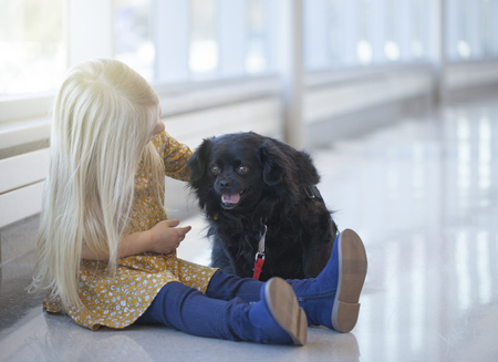 Portrait of little girl sitting on floor and stroking black dogの写真素材