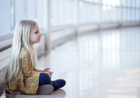 Portrait of lonely little girl in yellow dress sitting on floorの写真素材