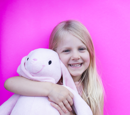 Happy little girl holding toy bunny on colorful backgroundの写真素材