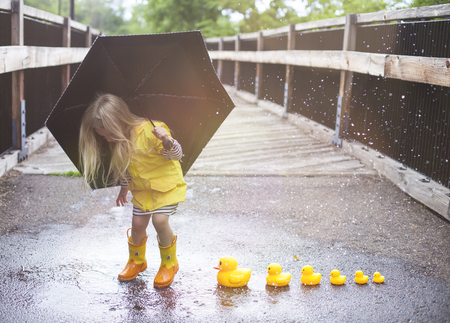 Joyful girl jumping on puddle with ducks next to itの写真素材
