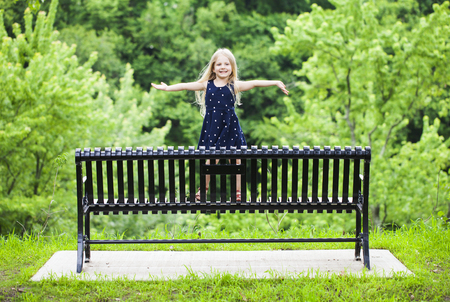 Portrait of happy cute little girl standing on metal bench in parkの写真素材