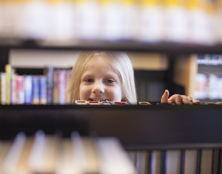 Happy face of schoolgirl between shelves in the library
