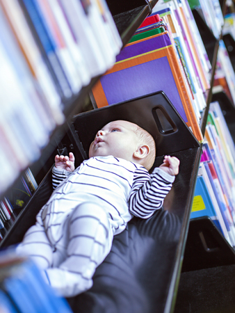 Little baby in library lying on shelf among books in libraryの写真素材