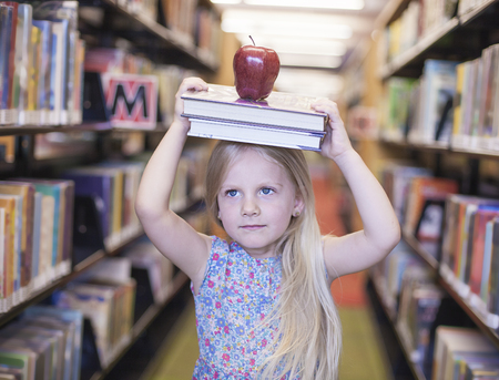 Cheerful schoolgirl holding the books with apple above her head. Education or back to school or wisdom conceptの写真素材