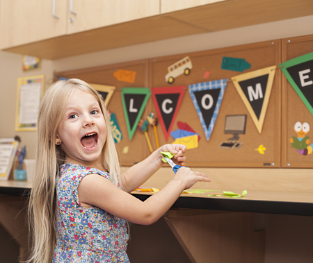 Smart happy girl cutting paper, making craft, Welcome back to schoolの写真素材