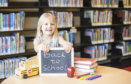 Cheerful girl holding chalkboard with words. Back to school in the libraryの写真素材
