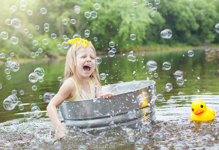 Laughing small girl in metal bathtub in the river at summer timeの写真素材