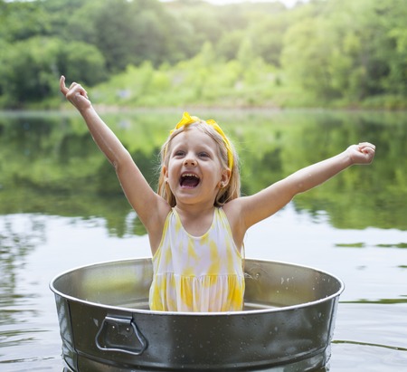 Laughing small girl in metal bathtub in the river at summer timeの写真素材