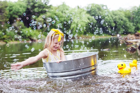 Laughing small girl in metal bathtub in the river at summer timeの写真素材