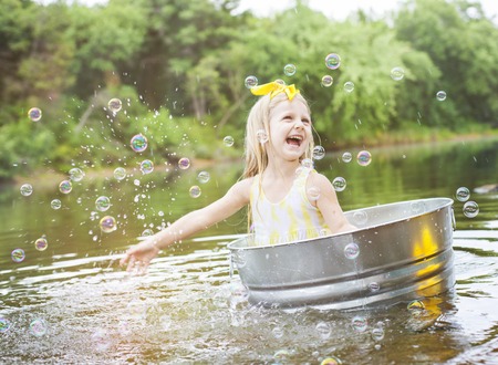 Laughing small girl in metal bathtub in the river at summer timeの写真素材