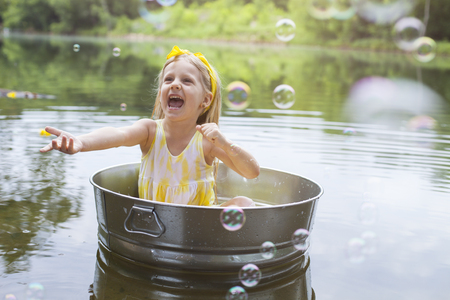 Laughing small girl in metal bathtub in the river at summer timeの写真素材