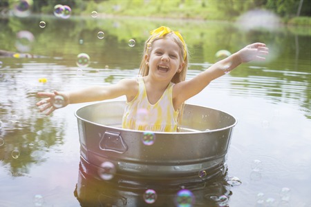 Laughing small girl in metal bathtub in the river at summer timeの写真素材