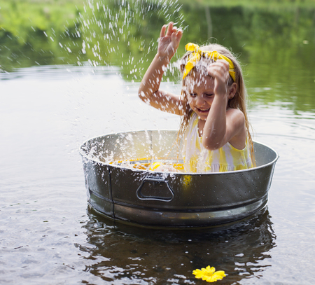 Laughing small girl in metal bathtub in the river at summer timeの写真素材