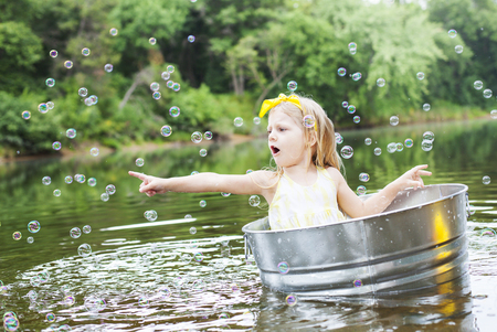 Laughing small girl in metal bathtub in the river at summer timeの写真素材