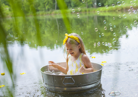 Laughing small girl in metal bathtub in the river at summer timeの写真素材
